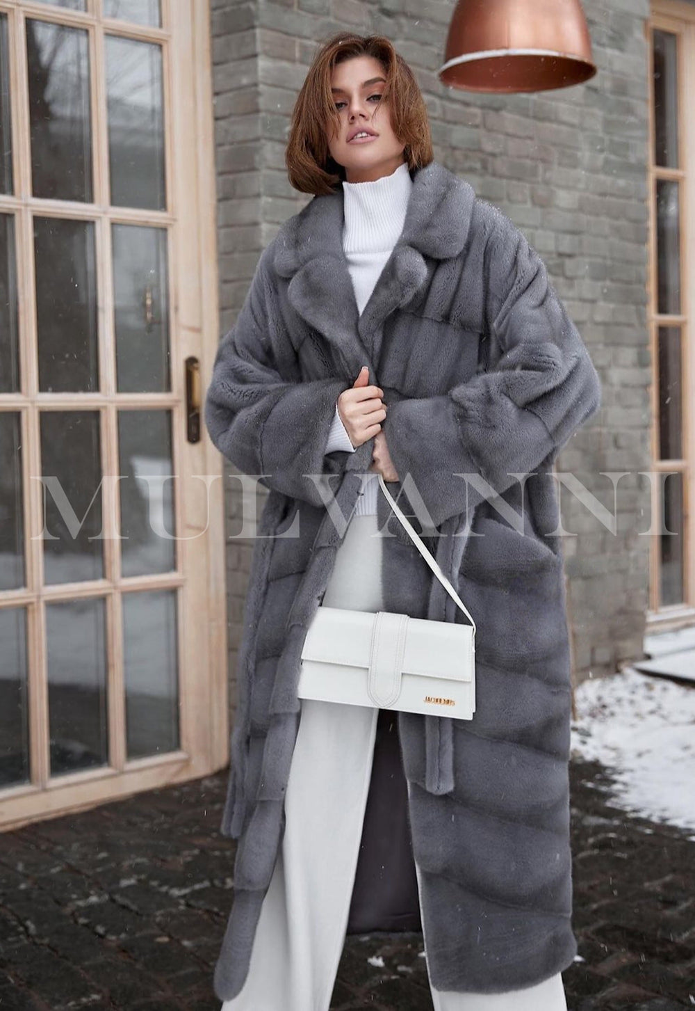 A woman dressed in a refined long grey mink fur coat, showcasing its plush texture and elegant design. The coat offers both warmth and a sophisticated look, perfect for cold-weather events.